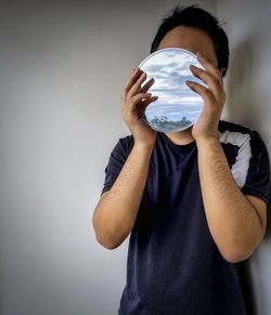 Portrait of young man holding covering face against wall