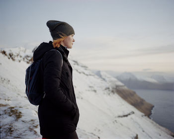 Woman standing on snowy mountain top looking out towards ocean