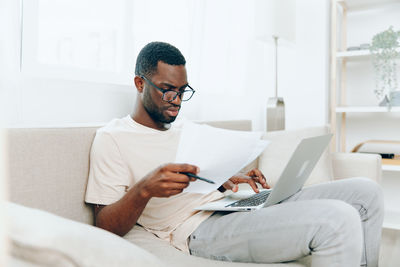 Young woman using laptop while sitting on bed at home