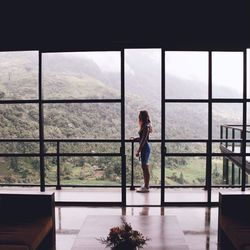 Woman standing by railing in balcony seen from window