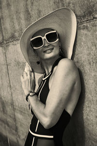 Portrait of a woman in a swimsuit, hat and sunglasses in summer on the riverbank by a concrete wall