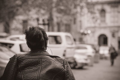 Rear view of woman wearing leather jacket standing on street in city