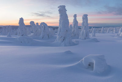 Snow covered landscape against sky during sunset