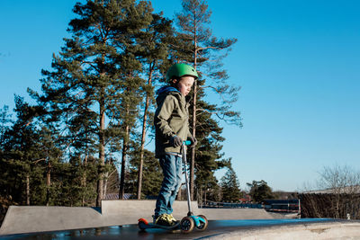 Boy standing on his scooter in a skatepark in the sunshine