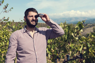 Man looking through refractometer while standing against plants and sky