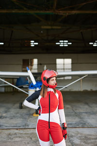 Young female skydiver in a plane hangar with a plane behind her