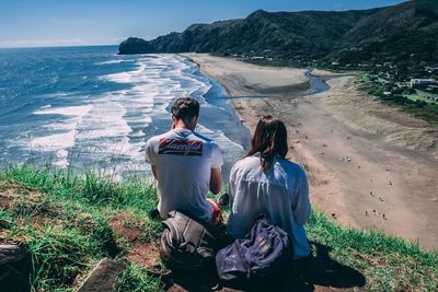 Rear view of friends sitting on beach against sea