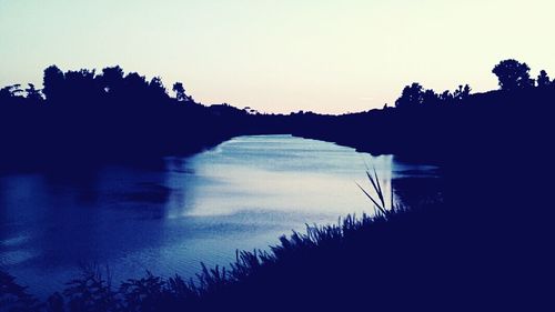 Silhouette trees by lake against sky during sunset