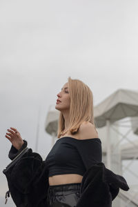 Side view of young woman standing against sky