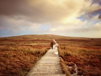 Rear view of person walking on boardwalk leading towards black mountain