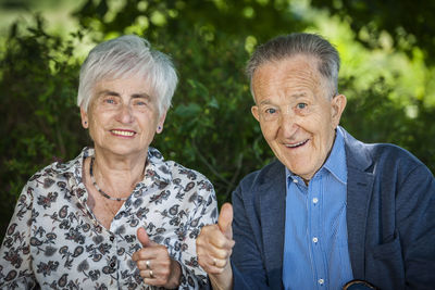 Portrait of an 80 year old retired couple showing the thumbs up and friendly looking at the camera.