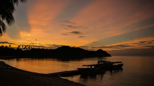 Silhouette boats in sea against orange sky