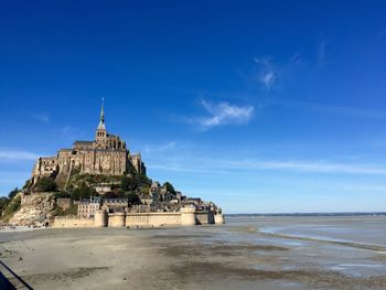 Mount saint michel on beach against blue sky