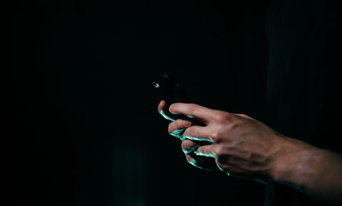 Close-up of hands holding mobile phone against black background