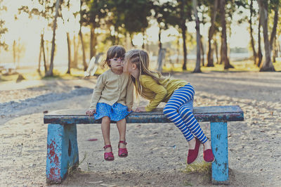 Girl kissing sister while sitting on bench at park