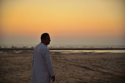 Man standing on beach against sky during sunset