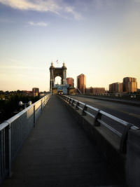 Walkway leading towards bridge over river in city against sky