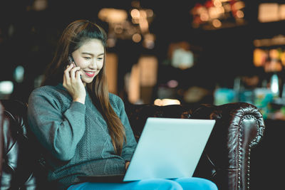 Smiling young woman using phone while looking at camera