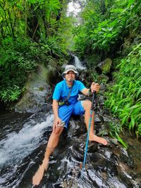 Full length of man sitting in stream at forest