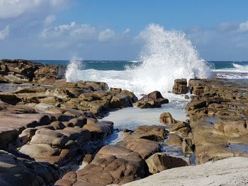 Waves splashing on rocks at shore against sky