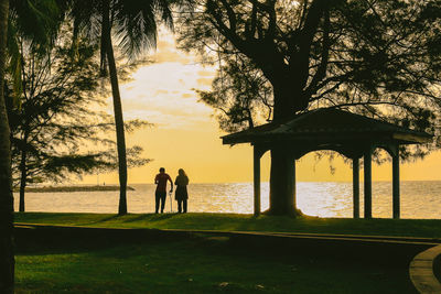 Silhouette people standing by tree against sky during sunset