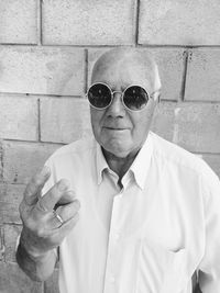 Portrait of senior man wearing sunglasses while standing against wall