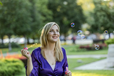 Beautiful blonde with long hair and long purple dress is balancing in public park. 