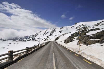 Empty road leading towards snowcapped mountains during winter