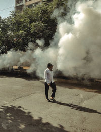 Side view of man walking on a street with visible air pollution, smoke and fog.