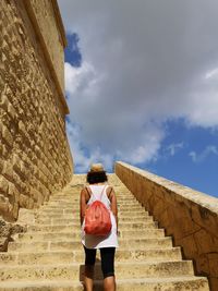 Rear view of woman walking on staircase against cloudy sky