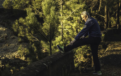 Side view of senior man exercising by tree in forest