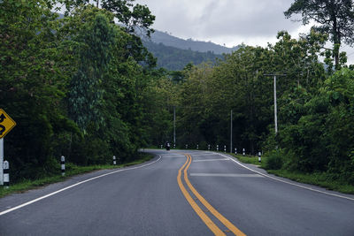 Country road amidst trees against sky