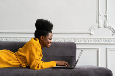 Smiling businesswoman using laptop while lying on sofa at home