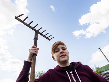 Portrait of boy holding gardening fork against sky