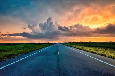 Road amidst field against sky during sunset