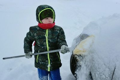 Boy using broom to remove snow from car