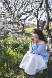 Woman standing by flower tree on field