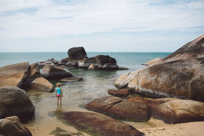 Woman standing in sea by rocks against sky