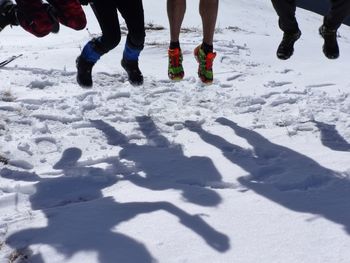 Low section of people jumping on snow covered field with shadows during winter