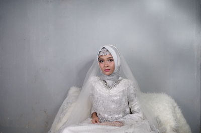 Portrait of bride wearing traditional clothing sitting against wall