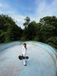 Musician girl  wears suit standing in the abandoned pool with the guitar on her hands in the forest.