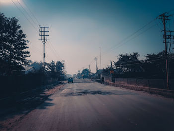 Road by electricity pylon in city against sky