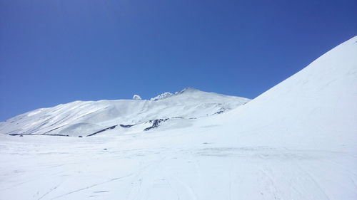 Low angle view of snowcapped mountains against clear blue sky