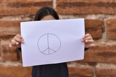 Close-up of girl holding paper against brick wall