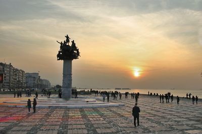 People in city by sea during sunset