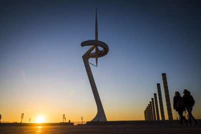 People walking by anella olimpica against sky during sunset