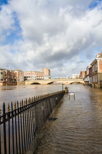 Pier over river by buildings in city against sky