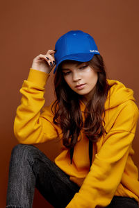 Beautiful young woman sitting against yellow wall