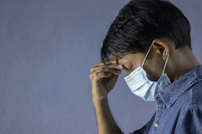 People, health problem and stress concept side face of a man suffering from headache with nose mask