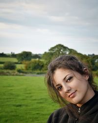 Close-up portrait of young woman on grassy field against sky